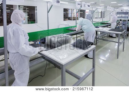 factory workers in white lab suits and face masks, producing tv sets on assebly line with some modern equipment