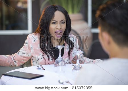 Black female disinterested with a blind date at an outdoor restaurant. They are sitting and chatting like speed dating. The image depicts relationship problems.