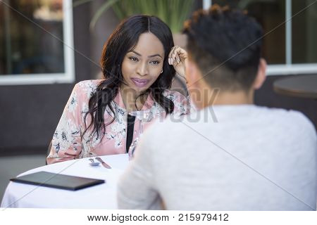 Black female disinterested with a blind date at an outdoor restaurant. They are sitting and chatting like speed dating. The image depicts relationship problems.