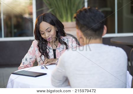 Black female disinterested with a blind date at an outdoor restaurant. They are sitting and chatting like speed dating. The image depicts relationship problems.