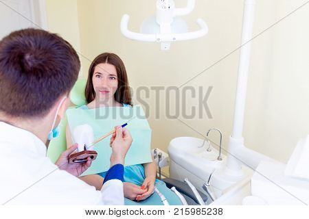 Young dentist male man with 3d model of one white big teeth explaining teeth treatment for young smiling female woman patient in dentist workplace in clinic