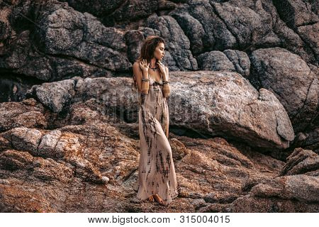 Beautiful Young Boho Style Woman On Stones Background At Sunset