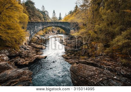 Golden Trees Surround The Road Bridge Over The Moriston River At Invermoriston In Scotland With A Sm