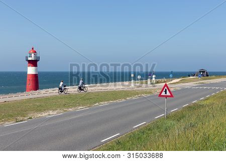 Westkapelle, The Netherlands - June 28, 2019: Lighthouse At Dike With Passing Bikers Near Westkapell