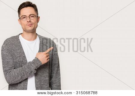 Sceptic Guy Pose On Grey Background Pointing Finger Aside Copyspace