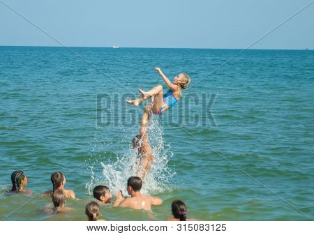 Odesa Rgn. Ukraine, July 29, 2018: A Young Man Throws Up A Girl In The Sea, And She Jumps Into The W