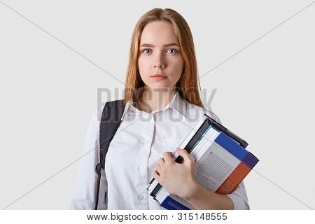 Studio Of Serious Caucasian Fair Haired Young Woman With Paper Folder In Hands, Wearing White Blouse