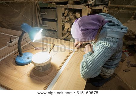 Woman Joiner Cleans  And Putty Spats Surface Of Door Leaf In The Carpentry Shop. Woman Working In Th