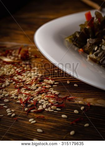 Rosemary And Sesame Spices Near White Plate On Wooden Background