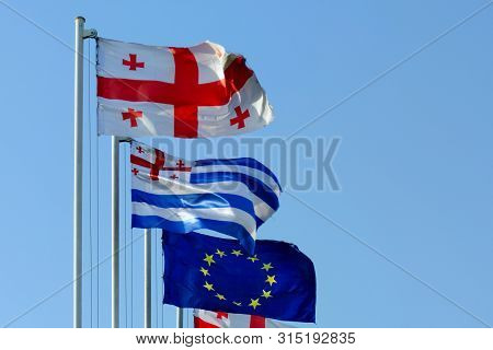 Flags Of Georgia, Ajaria And The European Union Fluttering In The Wind Against A Blue Sky.