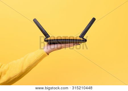 Black Wifi Router On Female Hand Over Yellow Background
