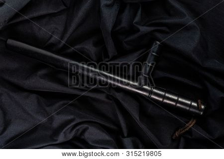 Black Rubber Police Baton On Black Shirt Wrinkled Cloth Low-key Flat Lay