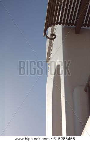 Part Of The White Wall With Arch, Balcony And Canopy Against The Blue Summer Sky