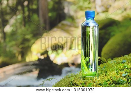 Plastic Bottle Blue Cap With Fresh Drinking Water On A Background Of Green Forest Stands On A Stone 