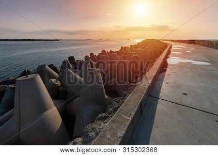 North Pier With Breakwaters, Sunset Seascape. Modern Lighthouse In Sunlight. Tetrapods Along Edges O