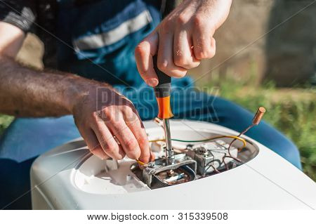 Repair And Maintenance Of The Water Heater. A Man Twists A Screwdriver Element Of The Water Heater. 
