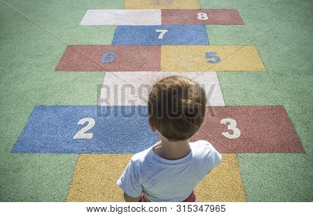 Boy Learning Numbers At Rubber Hopscotch. Numbers On The Pavement. Early Education At Mathematics An