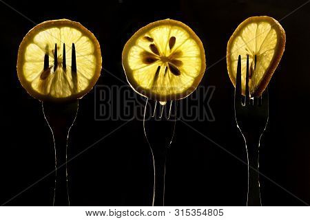 Collage Of Three Slices Of Lemons On The Fork On Dark Black Background. Silhouette Of A Fork In The 