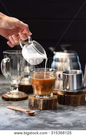 Woman Hand Pouring Coconut Cream Into Vietnamese Drip Coffee In Glass On Wood Slab On Dark Backgroun