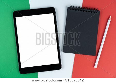 Black Tablet, E-book, Notebook And White Pencil Is On Flag Italy. Texture Italian National Flag Colo