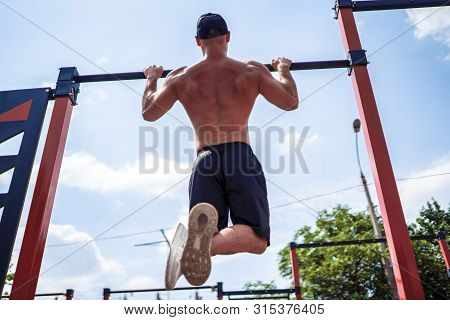 Brutal Athletic Man Making Pull-up Exercises On A Crossbar At Outdoor Streeet Gym.