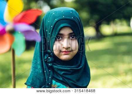 Portrait Of Happy Little Muslim Girls Child With Hijab Dress Smiling And Looking At Camera In The Pa