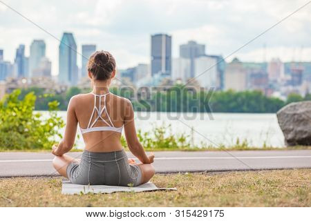 Zen yoga class outside in city park woman wellness meditating in lotus pose outdoor on mat and grass. Girl from behind sitting.