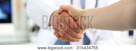 Focus On Male Shaking Hands. Physician Wearing White Uniform And Stethoscope. Men Demonstrating Welc
