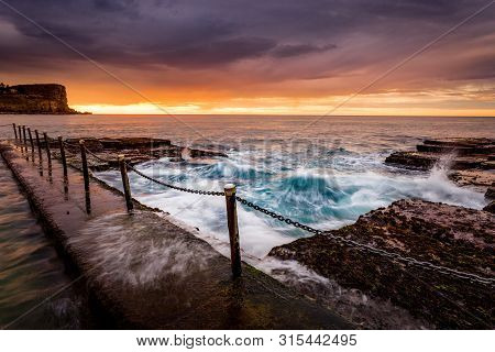 Coastal Sunrise By The Ocean Rock Pool  With Tidal Flows Over Rocks And Flowing Into The Pool