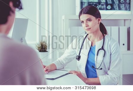 Doctor and patient discussing medical problems in a hospital consulting room. Doc filling in a patient's form