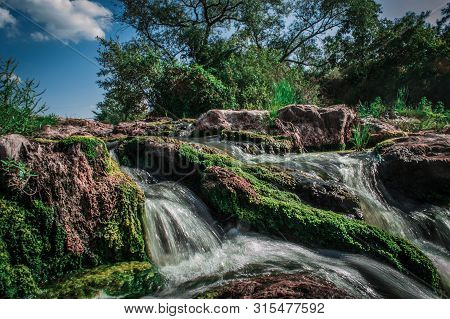 A Stream Flows Around The Stones. Stones Overgrown With Green And Brown Moss. Landscape With Trees, 