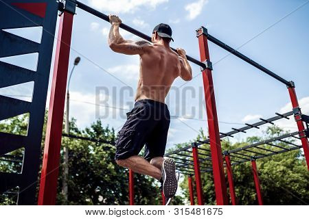 Brutal Athletic Man Making Pull-up Exercises On A Crossbar At Outdoor Streeet Gym.