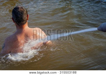In The Thermal Pool, A Man Receives A Back Hydromassage With A Powerful Jet From The Nozzle.