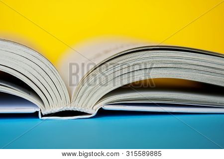 An Opened Thick Book Or Diary On A Yellow And Blue Background. College Or School Library. Close-up. 