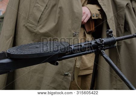 Soldier In A Green Cloak In Front Of A Wwii Machine Gun.