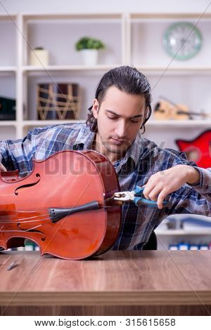 Young handsome repairman repairing cello