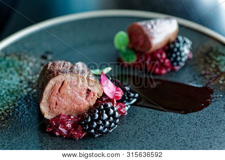Venison fillet with beetroot carpaccio and blackberries on dark plate