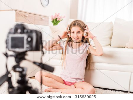 Young smiling videobloger teen girl is pointing at camera in living room