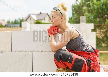 Woman Thinking About Future Of Building Her Home. Female Sitting On Wall Made Of Airbricks On Constr
