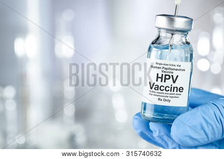 Healthcare concept with a hand in blue medical gloves holding HPV, human papillomavirus, vaccine vial