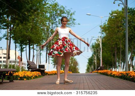 Full body portrait of a beautiful young brunette woman walking in flowers dress, summer park outdoors