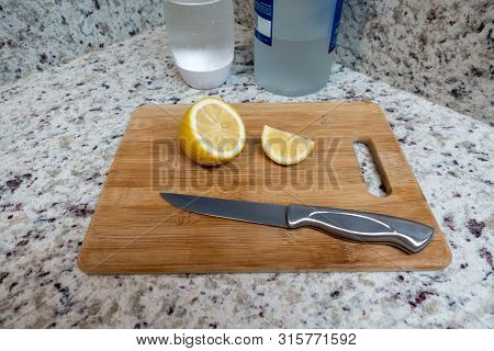 A Cut Lemon On A Wooden Cutting Board With A Knife, Soda Water And Alcohol Ready To Mix A Drink.