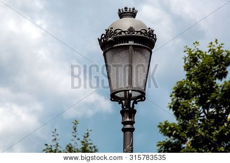 Black Iron Street Lamp In Retro Style With A Glass Shade In The Background In The Blur Sky With Clou