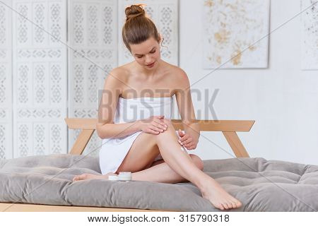 Cute Caucasian Woman In White Towel Applying Cream On Her Skin Before Spa Procedure On The White Sal
