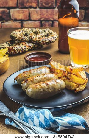 Meal For The Munich Oktoberfest With Sausages, Potato And Pretzels Served With Beer Over Rustic Wood