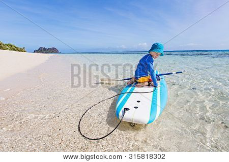 Little Kid In Rashguard Enjoying Stand Up Paddleboarding In Beautiful Turquoise Lagoon At Fiji Islan