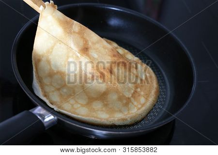 Baking Pancakes On Electric Induction Stove. Person Flips A Pancake With A Wooden Spatula In The Bla