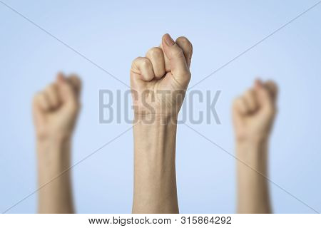 Female Hands Clenched Into A Fist And Raised Up On A Blue Background. Concept Of Power, Rebellion, U
