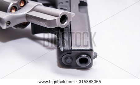 Two Handguns, A Silver Snub Nosed 357 Magnum Revolver And A Black 9mm Pistol On A White Background