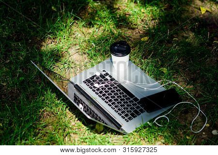 Laptop With Headset Of Mobile Phone And Coffee To Go On Green Grass. Agile Business. Online Study. S